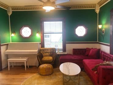 Stylish green living room with velvet seating, a white piano, and decorative accents.
