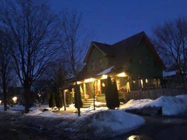 Charming green house illuminated at night with snow-covered yard and street.
