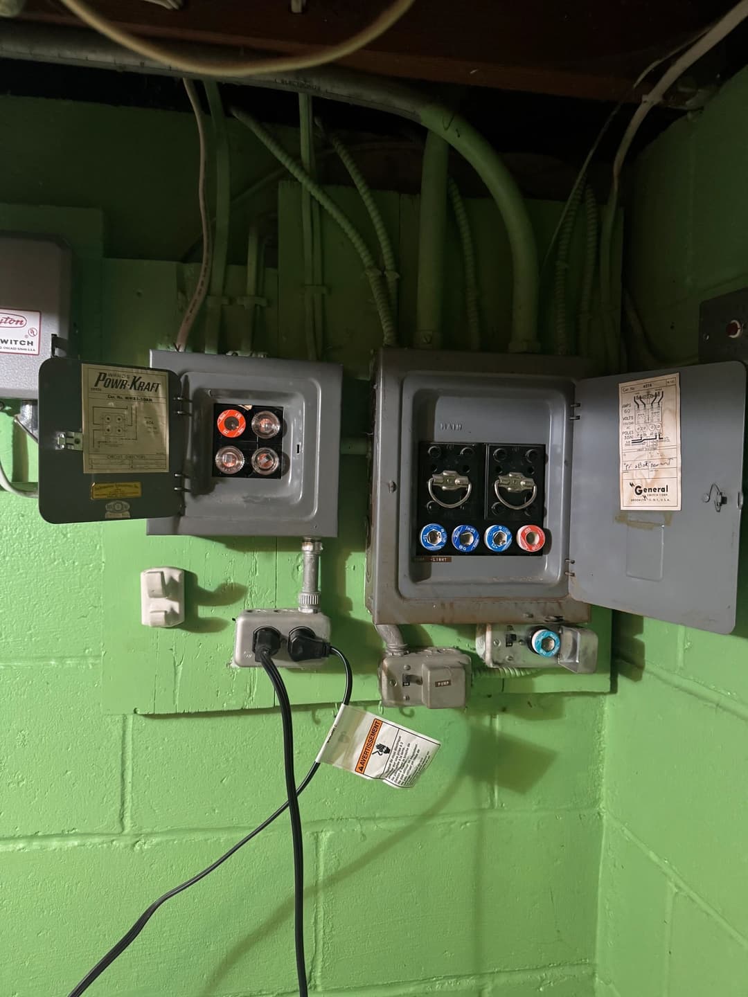 Electrical panel with two circuit breakers and wiring in a green basement.